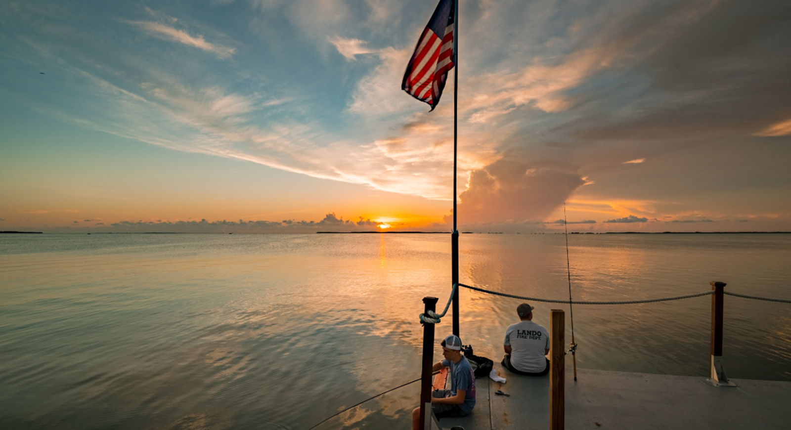 a man and a boy sitting on a boardwalk at sunset