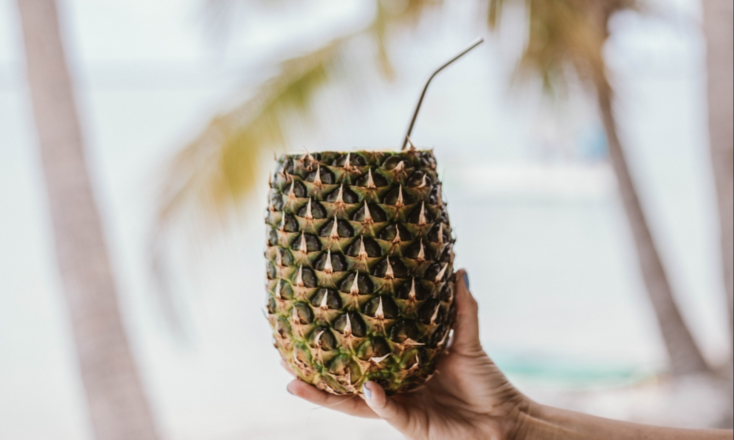 a hand holding a pineapple with a straw in it