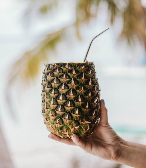 a hand holding a pineapple with a straw in it