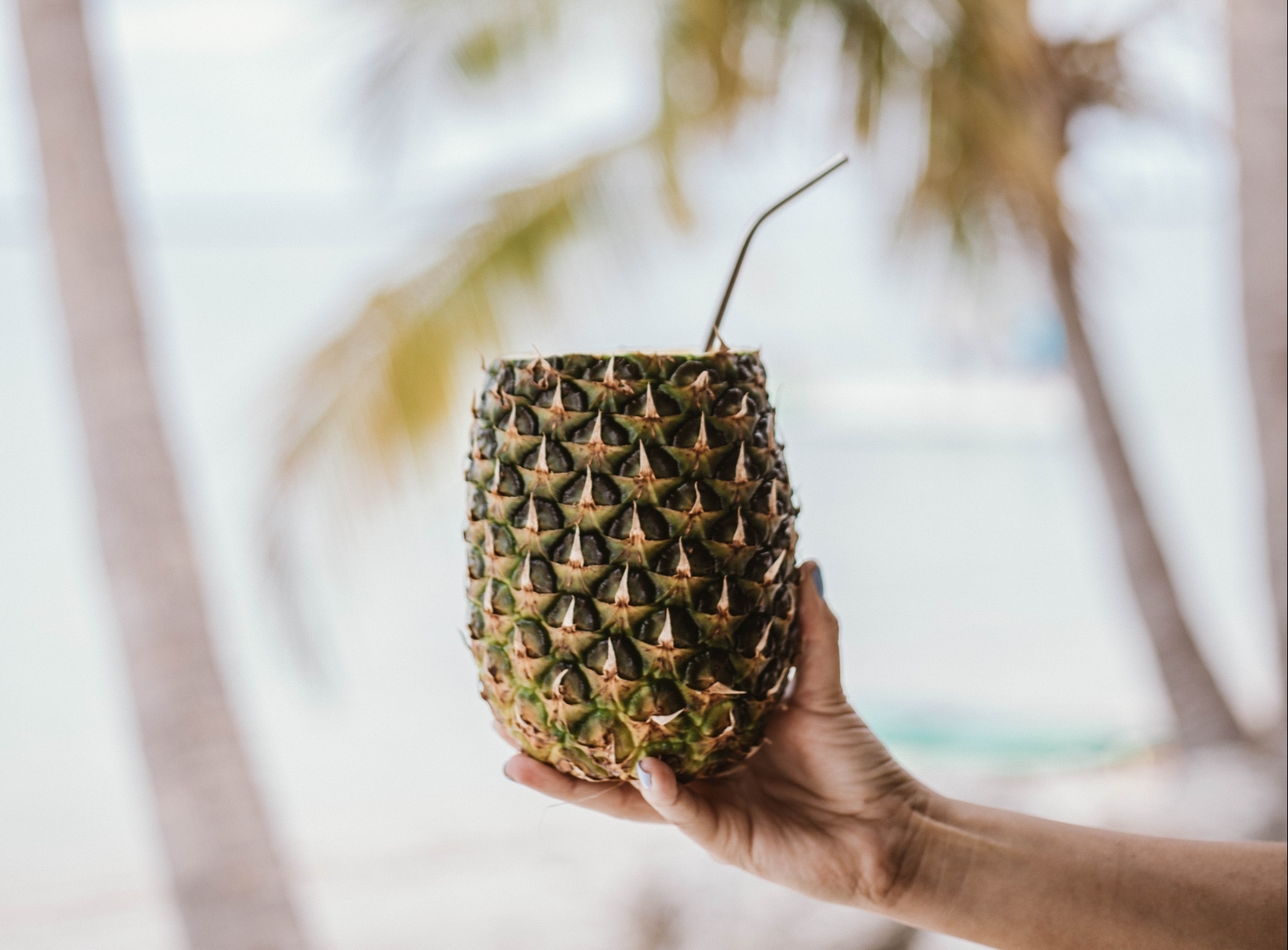 a hand holding a pineapple with a straw in it